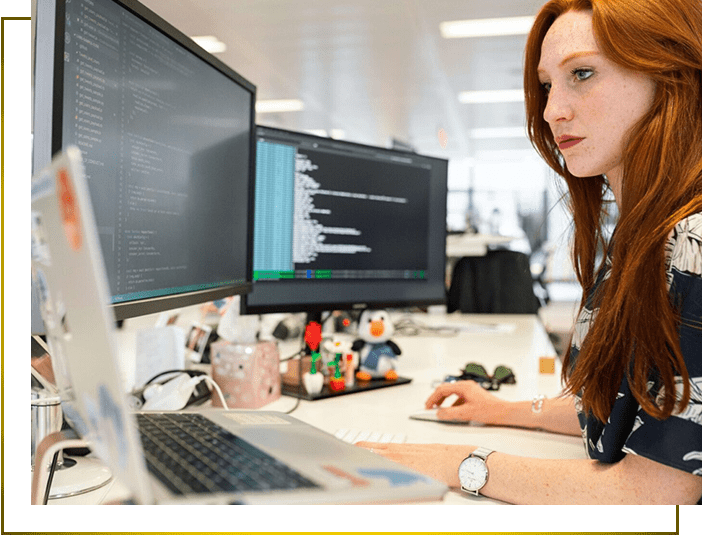 A woman sitting at her desk with two monitors.